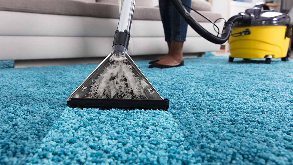 osoba čisti tepih u kući sa usisivačem